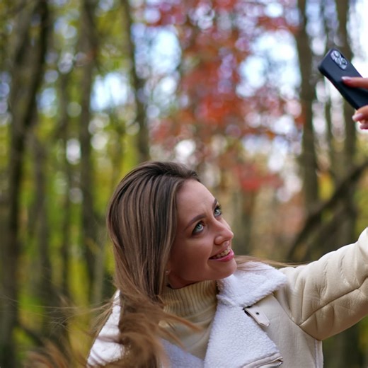 Attractive long-haired brunette taking selfie on her phone. Lady taking picture of herself in the autumn nature. Blurred backdrop | Premium Stock Video Footage