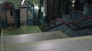 Nighttime view of a tiled subway entrance with blue doors and vibrant lighting, stairs leading to a platform
