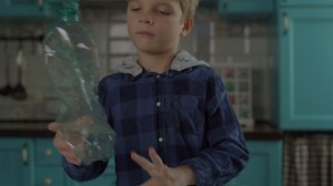 Preschool boy sorting plastic bottles into containers with green recycle sign. Home recycling process. Easy to recycle.