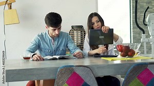 Young couple talking using tablet and reading magazine sitting by table at home
