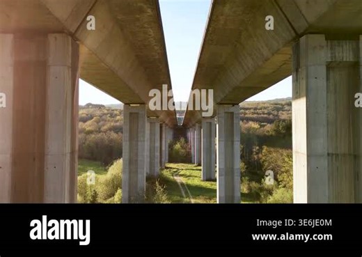 Symmetric view from underneath a concrete highway viaduct with supporting pillars over a valley Stock Video Footage - Alamy