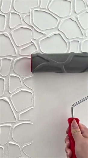 The person is rolling a patterned paint roller to create texture