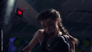Beautiful young tanned woman punching bag in fitness studio. Boxing in slowmotion.