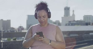 Plus size woman listening to music with headphones, exercising and using a phone to track weight loss in the city. Chubby active latino woman getting fit with a routine outdoor workout in town