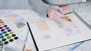 Baker is drawing the design of a birthday cake with watercolors.