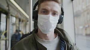 Young Guy Rides On Bus With Medical Mask On His Face. Guy Listening To Music Through Headphones. Protecting Health In An Epidemic.