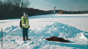 Happy beautiful 50s woman blowing snowflakes from her hands to her dog irish setter enjoying winter snow outdoors activity in winter day holiday. People and animals together having fun and smiling