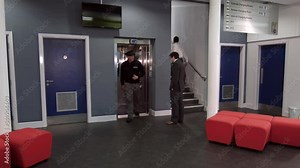Busy Office Building Lobby With Elevators And Stairs. Businessmen walking through the hallway as a security guard exits the elevator.