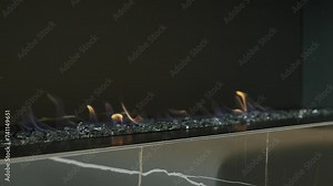 Close up of built into wall modern open fireplace burning with flames on ashes above black tiles with white veins in marble style pattern in living room