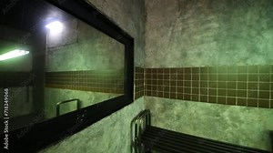 Swinging lamp in horrible dark room with mirror, bench and door.