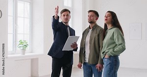 Realtor showing beautiful house to a young happy couple. Professional real estate agent showing new apartment. Successful family ready to become homeowners. Real estate market concept. 4k video.