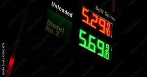 Gas station prices LED light up sign for regular and diesel fuel at night over 5 dollars per gallon price, during 2021 2022 war recession, ground up shot panning with telephone wires in background.