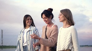 Three girls walking while one of them recording voice message on her smartphone.