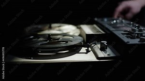 close up old reel-to-reel tape recorder plays magnetic tape record. Hand push start button. Beautiful gloomy shot of vintage retro turntable on table dark light. beam of light falls on old reel player