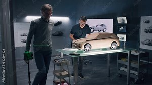 Two male automotive designers working on eco friendly model of electric car in modern car design studio. One sculpting with plasticine clay, other working in 3D modeling computer software.