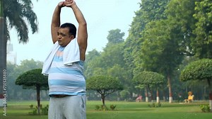Fat Indian man stretching his body in a public park - fitness morning routine unhealthy. Obese man stretching while doing a workout - overweight green park exercise outdoors wellness trying...