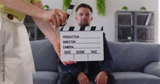 Close clapperboard slate marking film production in a home studio, where a director prepares an interview scene for cinema and calls a take. Clapperboard starts the interview scene now.