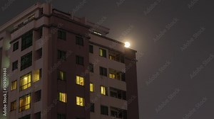 Time Lapse of Full Moon rising over a residential building as lights are switched off and on at night. The spectacular moon is revealed at the top the building. Part one of two clips
