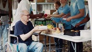 The needy are helped and fed by charitable group, and homeless people are given free food, including fresh fruit. Wheelchair-bound disabled man is given a warm meal from volunteer at a food drive.
