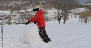 Boy crashes into snowman and breaks it. Child destroys big snowman and has fun. Winter holidays