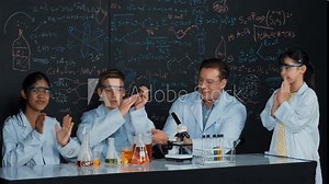 Multicultural student looking under microscope while cute girl inspect sample. Teacher looking after high school children doing experiment at blackboard with science theory in STEM class. Edification
