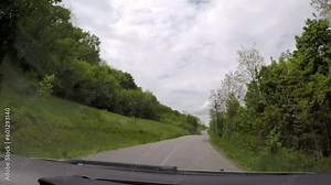 driving a car on a country road, hilly area, it's raining, it's spring, the road is wet, cloudy