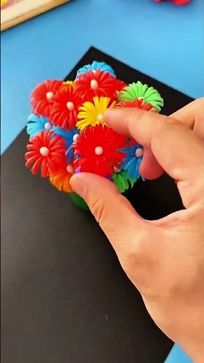Hands holding red artificial flower with white center, colorful flowers in background
