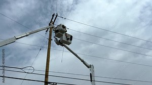 Power line work. Lineman crews work on power lines high in the sky. An elevated hydraulic bucket lifts the workers up to the power line. Overcast cloudy skies.
