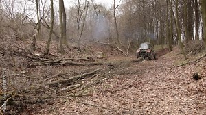 Skidder pulling logs on wood storage in forest. Spring has come in mountains after winter and heavy tracked tractors are pulling large tree trunks through mud.