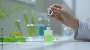 The template video in the tea tree experiment background, shows a front view of a white opaque serum bottle with green substance that was opening and dripping substance to be observed by a scientist.