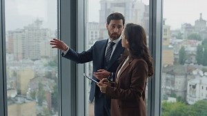 Serious businessteam discussing standing at office panoramic window close up. Attractive businesswoman holding folder making notes indoors. Businessman ceo working explaining business processes.