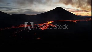 Glowing hot lava river flowing slowly over old lava field in sunset dim light. Aerial drone shot