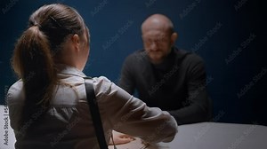 Female FBI agent interrogates suspected criminal in handcuffs. Police officer opens dossier folder with evidence. Detective asks question to detained guy without his lawyer. Law, justice. Victim