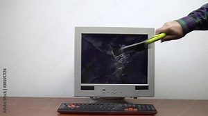 An old monitor sitting on a table is smashed with a hammer. The shattered glass of the monitor is flying in all directions. Slow motion.