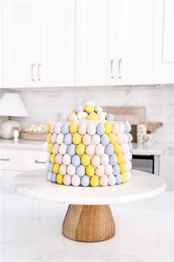 Decorating this Easter Egg Cake was so fun! While rushing through the grocery store, I spotted two vanilla cakes that seemed perfect for this edible DIY project. You can absolutely bake your own cake, but this time-saving hack means you don’t have to bake or wait for it to cool before assembling. This trick can save you anywhere from one to three hours! Whether you go with store-bought or homemade, decorating with colorful chocolate eggs is so much fun. And as you can imagine, it was just as enj