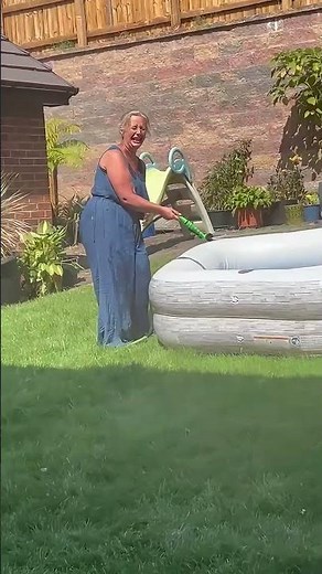 Woman struggles to control runaway garden hose while filling paddling pool in England, UK