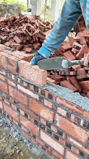 building the red brick wall using a grey cement and the blue gloves for the construction activity