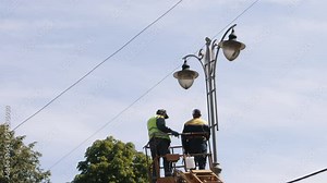 Municipal worker, repair street lamp, aerial device. Repair work at street light, worker fixing light pole lamp at height while wearing personal protective equipment, replacement of led lights