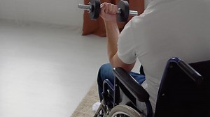 Disabled athlete in wheelchair performs exercises with dumbbells, home training and physical activity