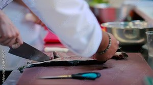 Close-up: the woman preparing a fish at the kitchen of the restaurant. Chef teaches how to cut a knife fish bones in the fish fillet. The female hands cuts the fish on the cutting board.