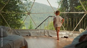 Child exercises by panoramic window at glamping. Little boy does yoga standing in clear camp cabin. Cute kid sports activity on family vacation