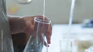 A woman pours a special solution from a vessel with a dispenser into a glass flask. Work in the laboratory. The worker carries out tests.