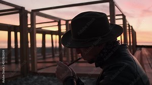 Portrait of a Man in a hat and leather jacket Smoking a cigar at sunset. The man lights a cigar and blows smoke. Close up.