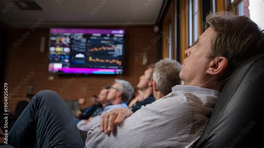 Medium shot of patrons seated comfortably while watching a digital display board update realtime queue status inside a hightraffic service venue.