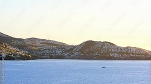 White Aegean houses of Yalikavak next to sea, sunset and moving boat in see at Bodrum, Turkey. Bodrum is most popular summer vacation area for tourist in Turkey.