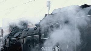 Vintage black steam locomotive. Historic train runs through fields. Vehicle departs from railway station. Old steam train locomotive is leaving the railway station.