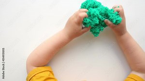 Baby Hands Playing with textured slime with bubbles, stretching the gooey substance on white background. Little child hand holding green shining slime toy squeezing it to the sides. Top View 4K video