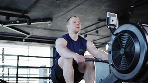 Strong middle aged man doing exercise with rope pull machine and resting after set in gym, tracking left medium shot