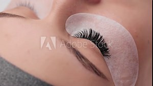 Eyelash extension procedure. Professional beauty master combing female lashes with special mascara brush. Fake eyelashes. Eyelashes extensions close up. Makeup artist and client in beauty salon.