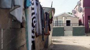 Clothes dry on a washing line next to a cinder block wall in a dusty township location.
